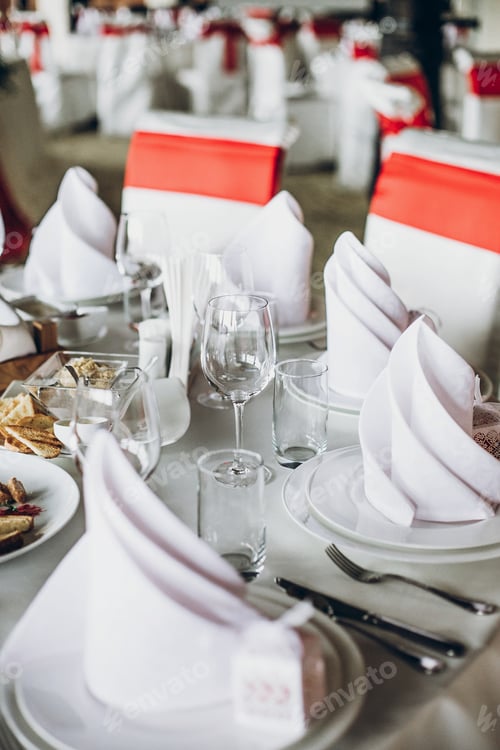 Preview: Wedding table with food, silver cutlery, empty glasses, white silk chairs and napkins