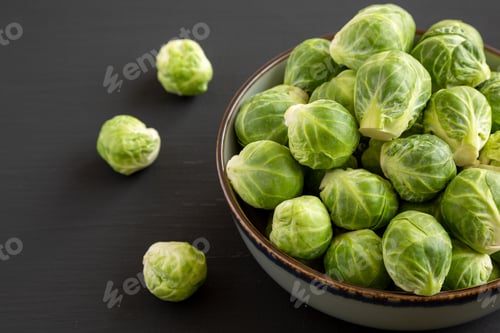 Preview: Raw Organic Brussel Sprouts in a Bowl on a black background, side view.