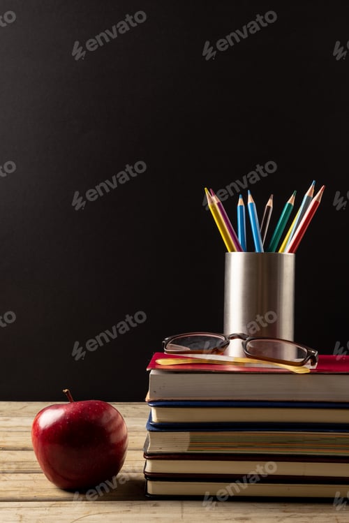 Preview: Vertical image of books, glasses, crayons in container and apple on black surface