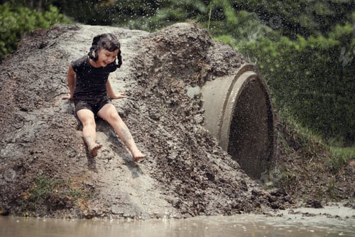 Preview: Cheerful child girl playing on heap of wet soil during raining in rainy season.