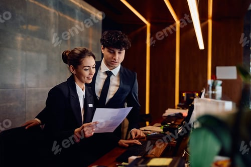 Preview: Hotel managers cooperating while going through paperwork at reception desk.