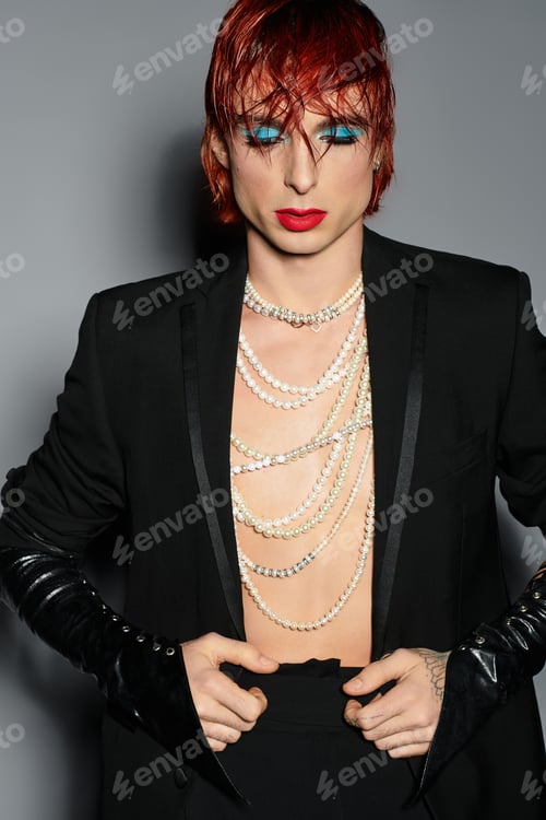 Preview: A young man with red hair wears bold blue makeup and elegant attire in a stylish setting.