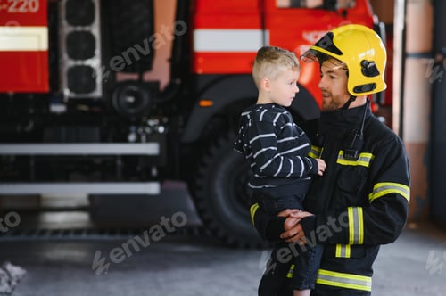 Preview: Dirty firefighter in uniform holding little saved boy standing on black background.