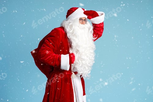 Preview: Santa Claus holding bag with gifts looking away, hurry up isolated on blue background with snow