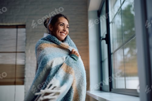 Preview: Young happy woman wrapped in a warm blanket at home.