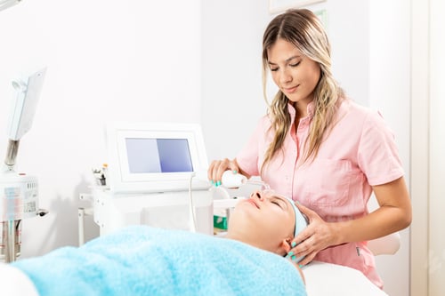 Preview: Beautician therapist applying face treatment in beauty salon to young woman.