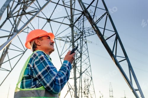 Preview: Electrician talking on portable radio device near high voltage tower