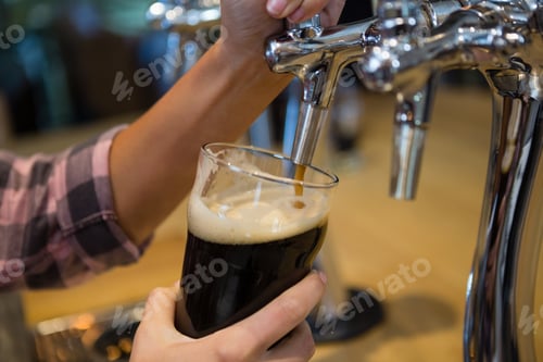 Preview: Cropped hands of barmaid pouring drink from tap in glass