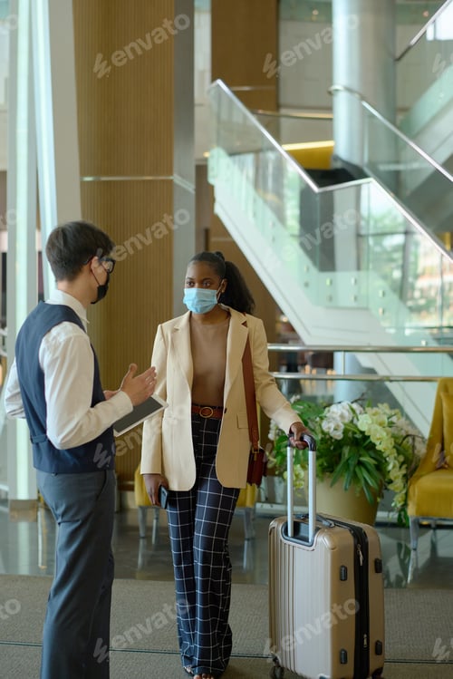 Preview: Young African American woman with baggage listening to male receptionist