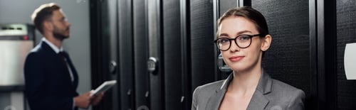 Preview: panoramic shot of attractive businesswoman in glasses looking at camera near bearded businessman in