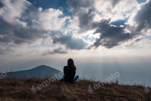 Preview: A woman sitting and watching sunset with mountains view in the evening