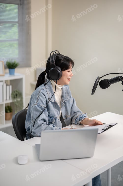 Preview: Asian woman with mic headset holding clipboard hosting radio podcast with laptop at home or studio.