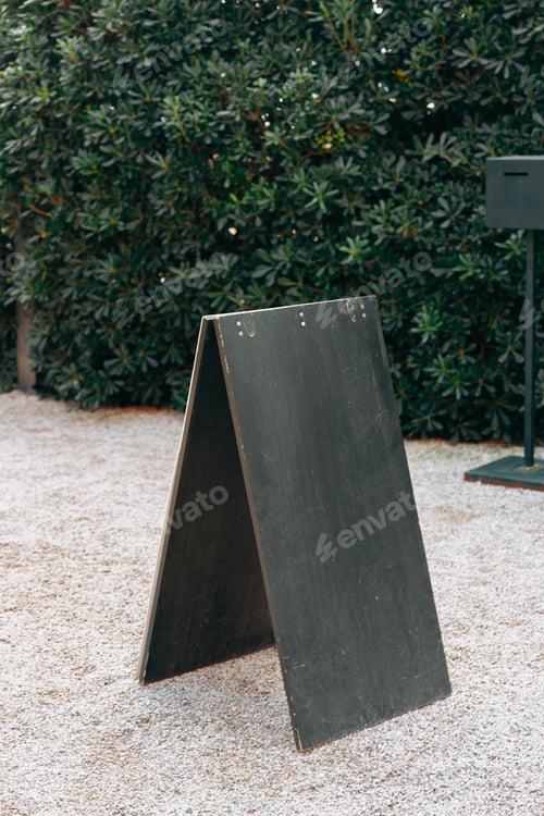 Preview: Sign board placed in a garden area near a black object during daytime