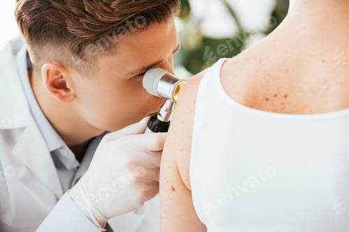Preview: dermatologist in latex gloves holding dermatoscope while examining patient with skin disease