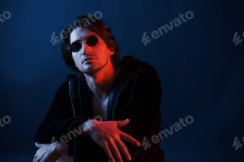 Preview: Beautiful man in glasses and black clothes is in the studio with blue neon lighting