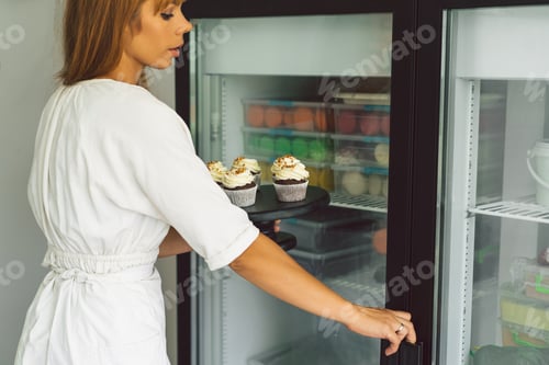 Preview: Confectioner girl is putting the cupcake in the freezer