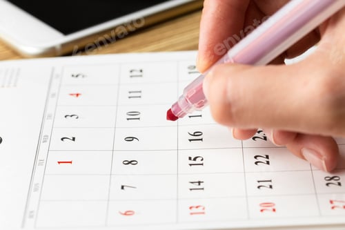 Preview: Marking important dates on a calendar with colorful pen in a bright workspace setting