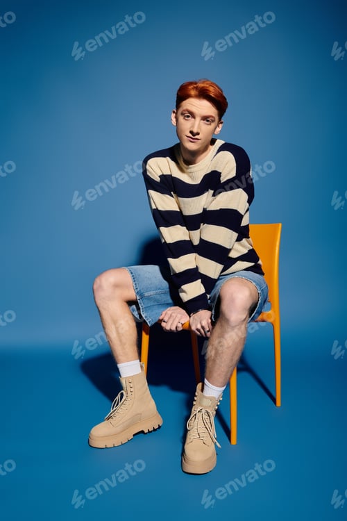 Preview: Emotional young man expressing feelings while seated on a bright chair in a vibrant studio