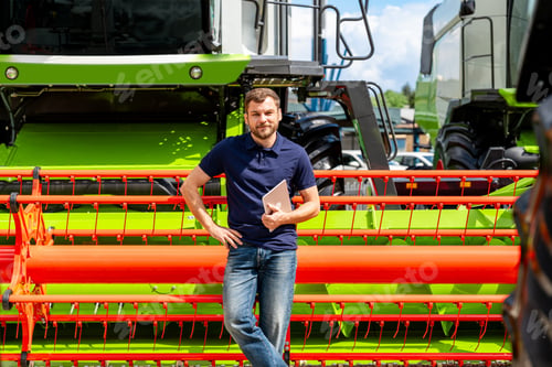 Preview: Male agricultural professional with digital tablet by combine header at outdoor equipment dealership