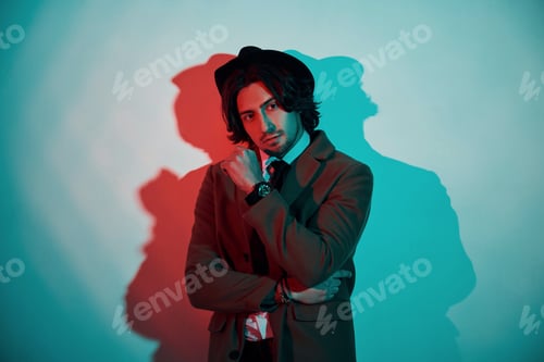 Preview: Portrait of young stylish man in hat, suit and tie that stands in neon lights in the studio