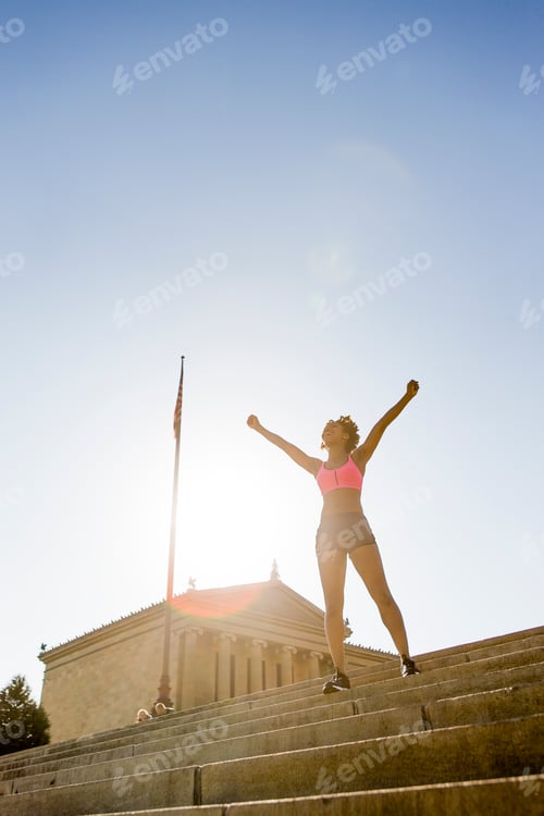 Preview: Young woman exercising outdoors, standing on steps, arms raised
