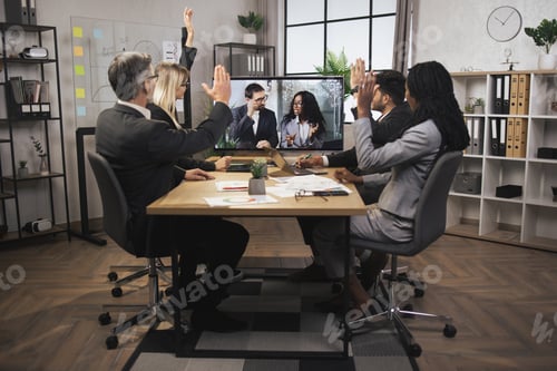 Preview: Smiling cheerful multiracial businesspeople sit at office desk, vote for the successful project