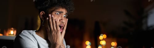 Preview: Young guy looking terrified while watching horror movie alone using laptop and eating popcorn