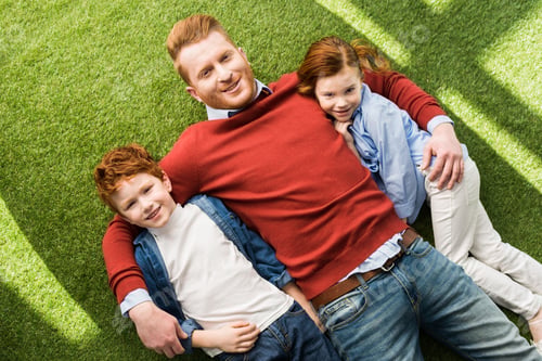 Preview: top view of happy father with adorable little kids lying together on grass and smiling at camera