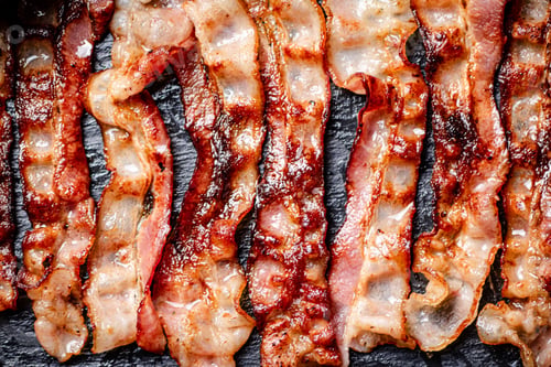 Preview: Strips of fried bacon on a black background.