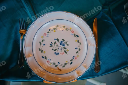 Preview: Top view of a ceramic plate with floral decorations on a table covered with blue cloth