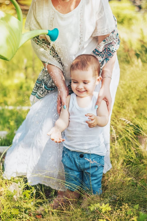 Preview: A little boy catches drops of water from a watering can in the garden with his mother.