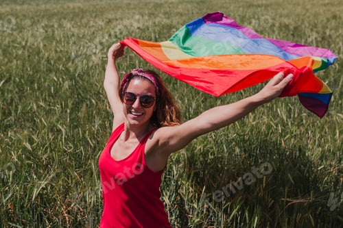Preview: Woman holding Gay Rainbow Flag on a green meadow outdoors. Happiness,freedom and love