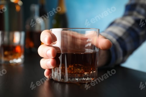 Preview: Male hand holds glass of whiskey on black table, close up