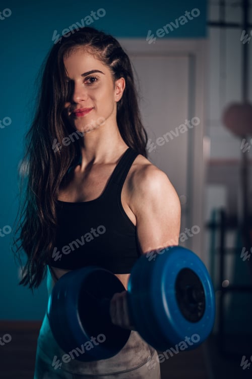 Preview: Gorgeous young woman holding dumbbells while training at home