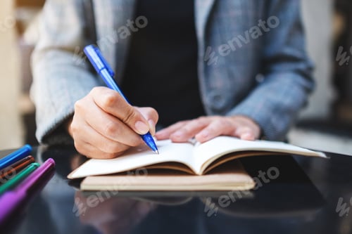 Preview: Closeup image of a woman writing on a blank notebook with colored pens on the table