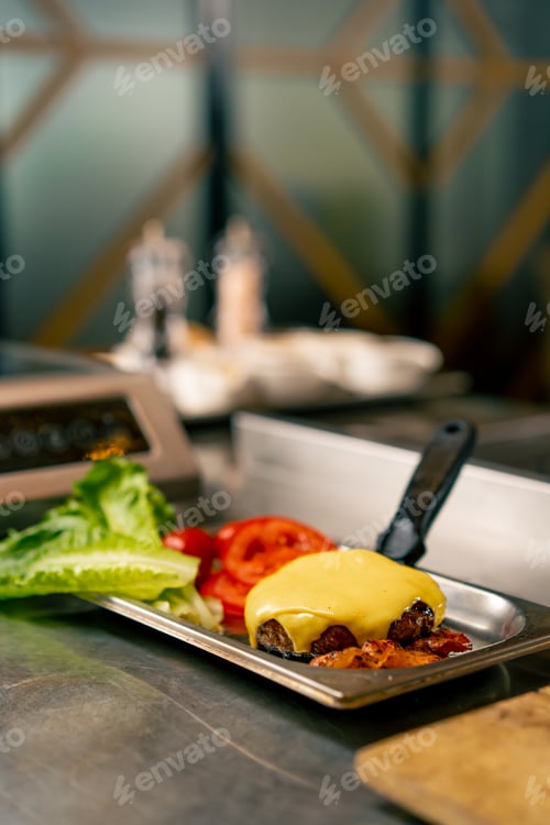 Preview: A close-up of a cooked beef cutlet with cheese lying on a kitchen spatula next to tomatoes and salad