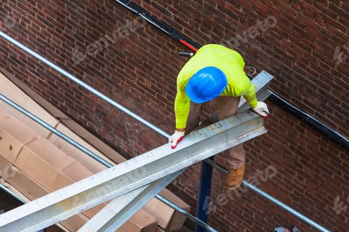 Preview: Worker in hard hat on a steel beam against a brick wall