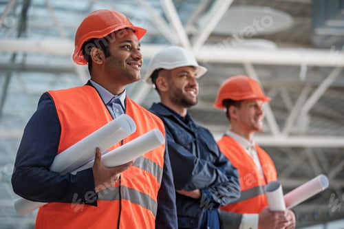 Preview: Cheerful Young Builders Are Working On Building Of Construction. Men In Helmets Are Standing And