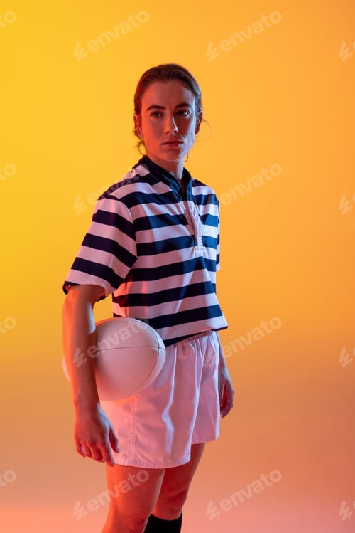 Preview: Portrait of caucasian female rugby player with rugby ball over neon yellow lighting