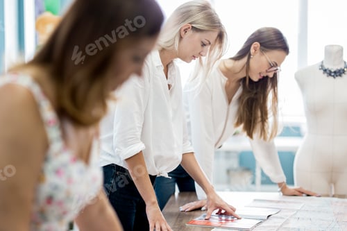 Preview: Three smart-looking pretty women are pointing at the sewing magazine. Fashion, tailor's workshop