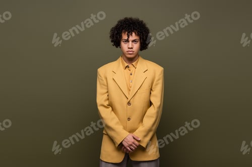 Preview: front view of young african american man with curly hair posing in yellow blazer on grey background
