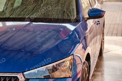 Preview: Close up hood and headlight of a blue car in a drops of water after car washing. Clean car after