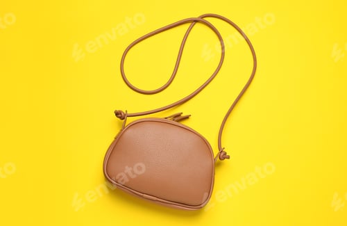 Preview: Stylish leather handbag on yellow background, top view