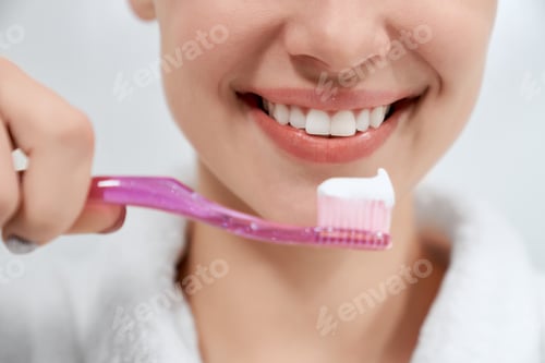 Preview: Woman cleaning teeth with pink toothbrush in bathroom.