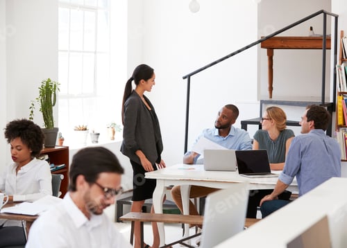 Preview: Woman talking with colleagues at a desk in open plan office