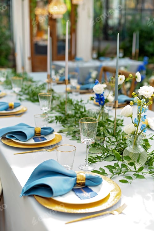 Preview: Banquet wedding table setting with blue napkins, gold cutlery, crystal, fresh flowers and candles.