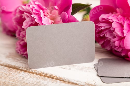 Preview: Gray business card with pink peony flowers on white wooden background. side view, copy space.