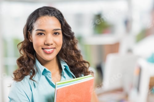 Preview: Office worker standing holding spiral-bound notebooks and colored folders in open-plan workspace