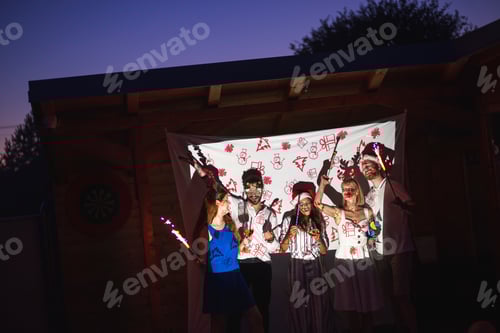 Vista previa: Amigos tocando silbatos de fiesta y saludando con bengalas en la fiesta de Año Nuevo