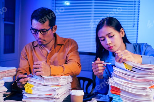 Preview: A businessman and woman are working overtime at their desks office at night.They are busy,stressed